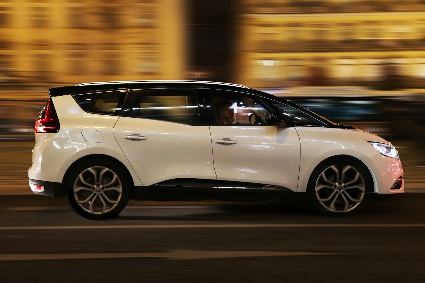 White modern car speeds down a city street at night.
