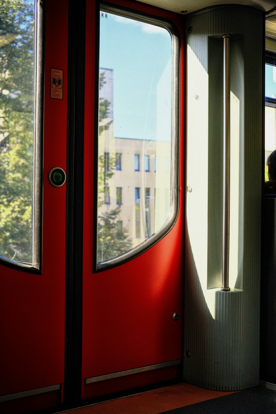 Red train doors open to a view of urban buildings.